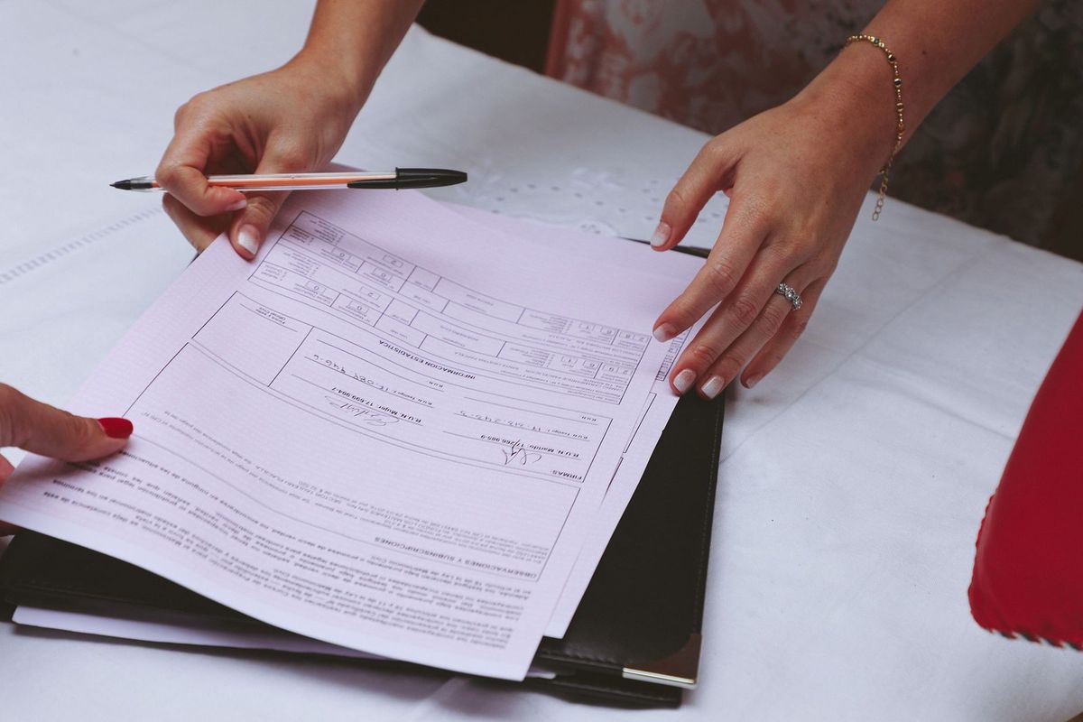 Deux mains signent un document sur une table, un stylo et un classeur à dossiers sont présents