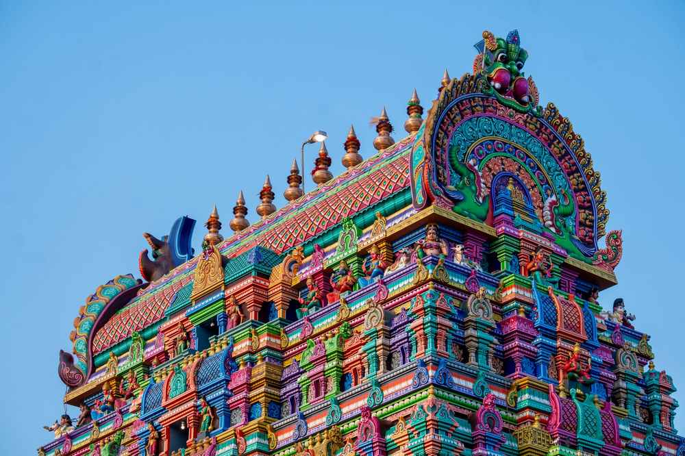 Tour colorée d'un temple hindou orné de sculptures sous ciel bleu