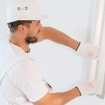 un ouvrier installe un panneau blanc sur un mur