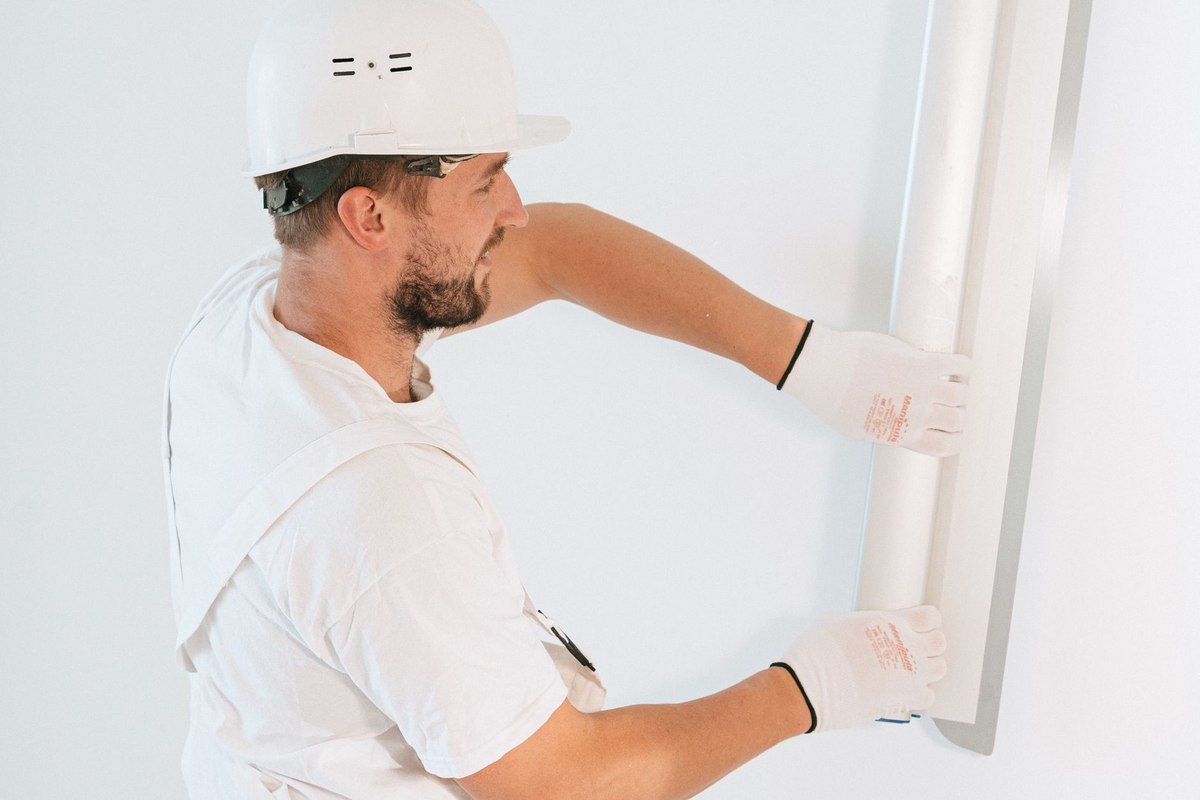 un ouvrier installe un panneau blanc sur un mur