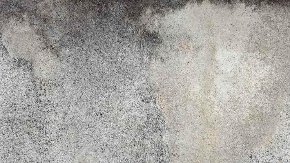Surface granuleuse d'un mur avec taches sombres et zones claires